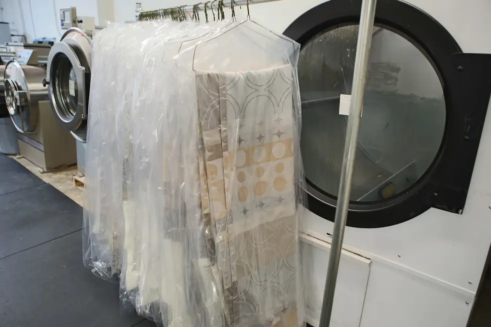 Rail of cleaned curtains in clear garment covers beside industrial washer drums