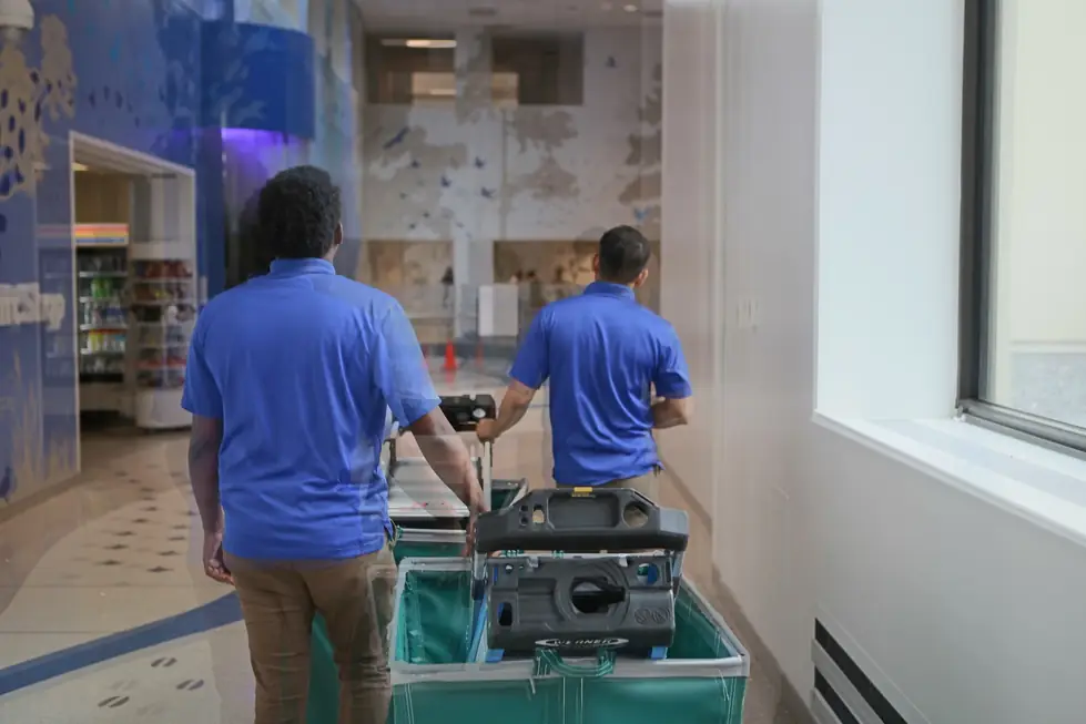Two installers in Accord polos pushing a green curtain cart down a hospital concourse
