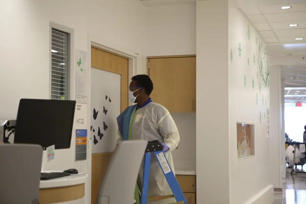 Installer in mask, gown and gloves carrying a ladder into a patient room